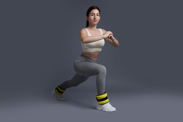 Woman in sportswear exercising with ankle weights on grey background