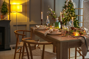 Christmas table setting with stylish dishware, glasses and burning candles in festive decorated room