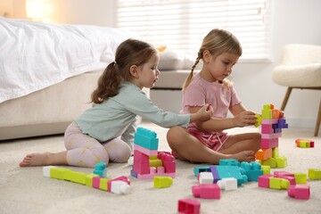 Naklejka premium Cute little sisters playing with colorful building blocks on floor at home