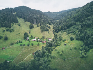 Aerial view of a lush green valley surrounded by forested hills under a cloudy sky.