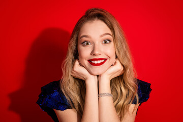 Joyful woman with radiant smile in glamorous attire posed against a vibrant red background,...
