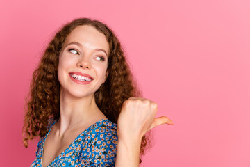 Cheerful woman in floral dress pointing over shoulder against pink backdrop