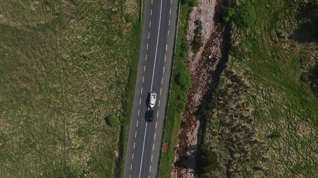 Barnesmore Gap, County Donegal, June 2023. Drone top down pan follows SUV car pulling boat along winding road through mountain pass alongside low river on a summer day