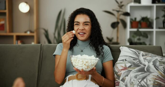 Woman, laugh or watching TV on sofa with popcorn, streaming service or enjoy comedy series in home. Girl, happy and snack in living room with funny movie, favorite sitcom and relax with entertainment