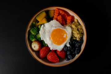 Vegetarian breakfast, Fried eggs, strawberries, blueberries, avocado, pumpkin, carrots, broccoli. on black background. Top view