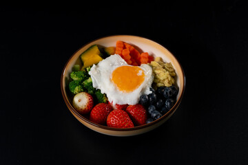 Vegetarian breakfast, Fried eggs, strawberries, blueberries, avocado, pumpkin, carrots, broccoli. on black background.
