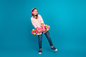 Adorable young girl with a pink skateboard posing against a bright blue background