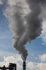 Chimney of a wood processing plant. Chimney with white smoke in a blue sky with white clouds