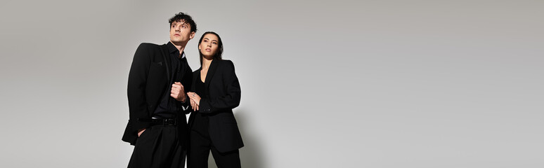 Stylish young duo posing confidently in trendy outfits against minimalistic backdrop