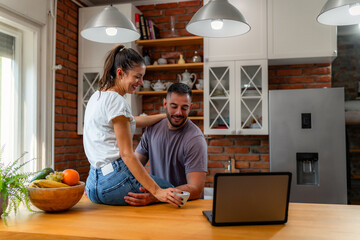 Kitchen conversation during work time. Woman perched on counter with coffee, sharing joyful moment with partner.