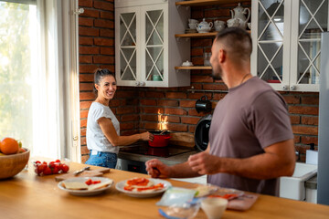 Young couple shares tender moment in morning kitchen, preparing fresh ingredients for their breakfast together.