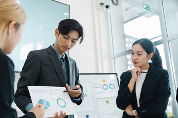 Focused Asian businessman presenting analytical reports to attentive colleagues in a modern office.