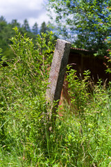 An old concrete post overgrown with grass and bushes. The remains of an abandoned and devastated garden fence.