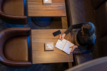 Woman writing notes at a table in a cozy cafe, overhead view of woman writing in a notebook at a table in a cafe.