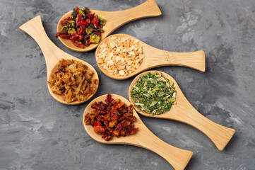Assortment of dried vegetables in small wooden spoons on a dark background, top view. Variety of spices and herbs.