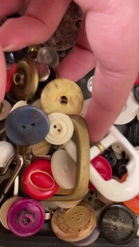 close up of a hand looking through a box of sewing buttons