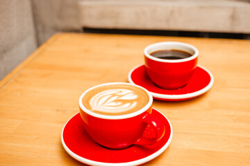 Cappuccino and Americano coffee in red cups on a wooden table