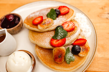 Pancakes with strawberries, fried bananas, ice cream and syrup on a wooden table. Delicious breakfast with fruits and berries