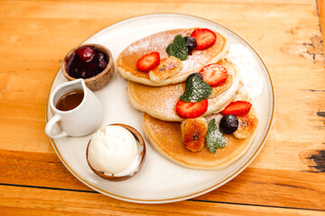 Pancakes with strawberries, fried bananas, ice cream and syrup on a wooden table. Delicious breakfast with fruits and berries