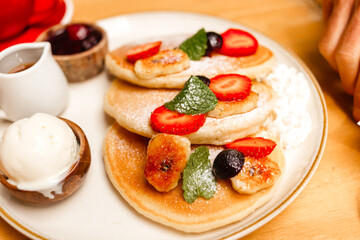 Pancakes with strawberries, fried bananas, ice cream and syrup on a wooden table. Delicious breakfast with fruits and berries