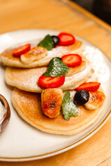 Pancakes with strawberries, fried bananas, ice cream and syrup on a wooden table. Delicious breakfast with fruits and berries