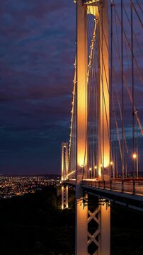 Wide Angle, capturing an iconic bridge spanning over lush hills during twilight hours with city lights beginning to twinkle in the distance, evoking excitement for urban adventures.