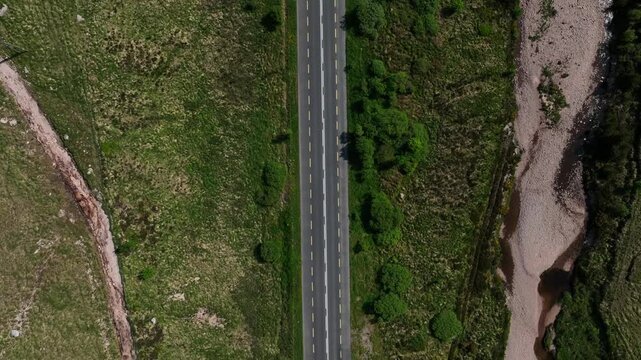 Barnesmore Gap, County Donegal, June 2023. Drone top down pan follows two lane traffic driving along winding mountain pass road bordering meandering river on a sunny day
