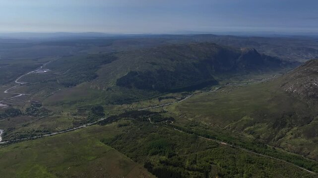 Barnesmore Gap, County Donegal, June 2023. Drone panoramic establishing overview above mountain peaks, connecting passage way with long road through boglands and forest on summer day