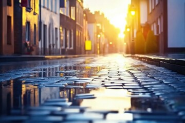 Obraz premium Vibrant cobblestone street at sunset reflecting warm golden light with puddles, creating a serene atmosphere, perfect for urban photography or travel imagery concept