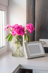 A vase with peonies next to a photo frame