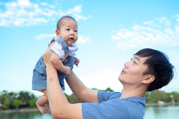 Father Joyfully Lifts His Baby in the Park Under a Sunny Sky With Clouds