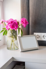 A vase with peonies next to a photo frame