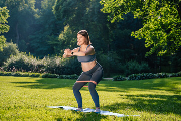 Pregnant young woman doing squats with a stretching band and looking focused