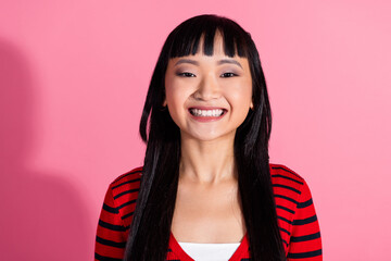 Smiling woman in a red striped cardigan against a pink background, displaying cheerful expression...