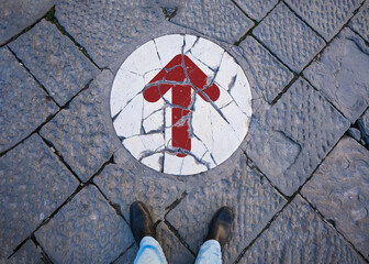 A person is standing in front of a Broken White Marble Slab in the floor. It has a circular shape and there is a sign of continuing with an arrow. Road, Decision and Going Concept