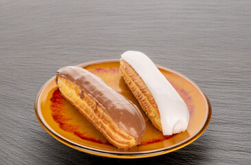 Two eclairs with cream filling on a ceramic saucer on a slate stone.