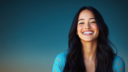 Smiling woman with long dark hair wearing a blue top against a gradient background at sunset