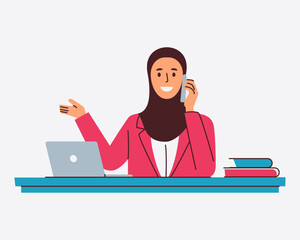 A smiling businesswoman in a hijab talks on her phone while gesturing towards a laptop on her desk