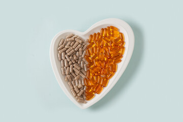 Medicinal herb, plant based supplements and omega oil pills in shape of heart on blue background. View from above. Healthcare concept.