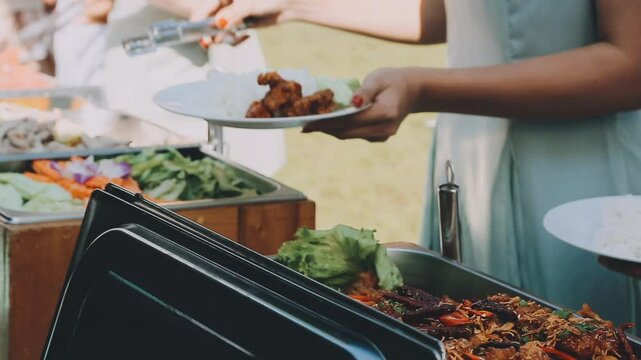 A group of people lined up to scoop up the food in the buffet line. Focusing on the hands of everyone who was scooping the food.