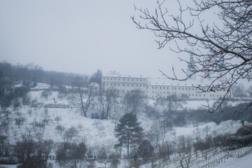 White misty view during snowy winter time in Prague towards Strahov monastery with gardens and dark...