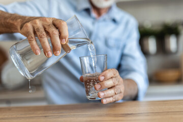 Senior man pouring water from the jug into glass in the kitchen. Senior man drinking water.