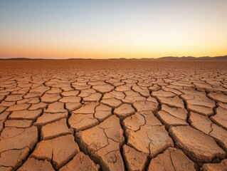 A vast, dry landscape with cracked earth under a clear sky, showcasing the effects of drought and arid conditions at sunset.