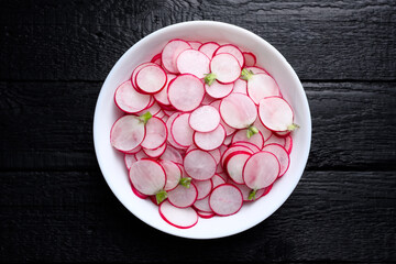 Radish slices in a white plate on black rustic wooden table. Vegetable salad. Food photography
