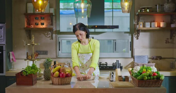 Indian asian gen x woman lady chef wear apron knead flour with hand indoor modern kitchen spend time young adult alone female mother mom bake food pastry dough bread on counter table enjoy day house