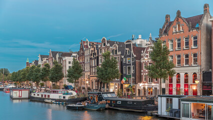 Fototapeta premium Panoramic timelapse hyperlapse of the illuminated famous Dancing Houses along the Amstel River day to night transition. Amsterdam, Netherlands