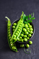 Green sugar snap peas with pods and leaf in a bowl on black background close up. Green pea beans vegetables. Food photography
