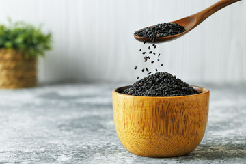 black sesame seeds falling from spoon in bowl on table