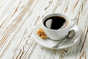 coffee in white cup on saucer with spoon and cane sugar cubes on wooden table