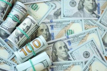 Many rolls of one hundred dollar bills lies on big amount of american currency banknotes